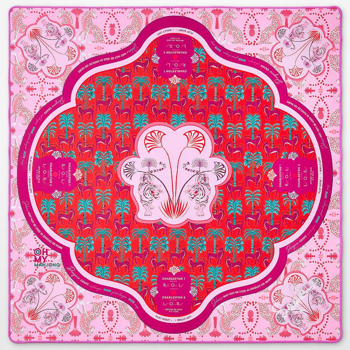 A square silk scarf laid flat, featuring a vibrant pink and red mandala design with intricate floral and botanical patterns. The central medallion is a rich red with a white border and pink floral motifs, surrounded by a wide pink border with additional decorative elements and text.