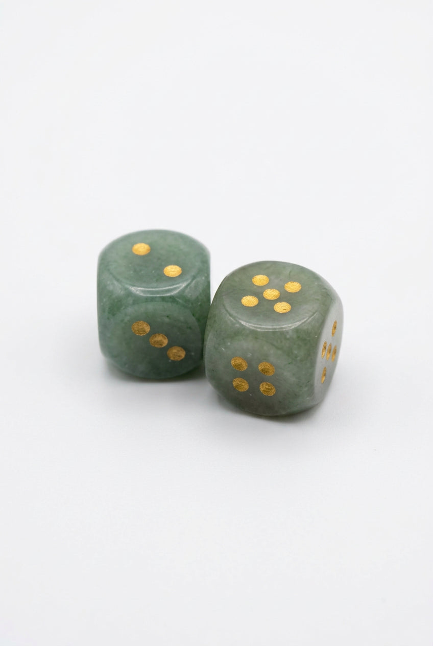 Two dark green dice with gold-colored dots, standing upright on a light gray textured surface.